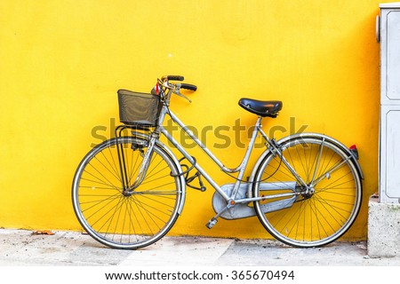 Old style bicycle parked against yellow wall.