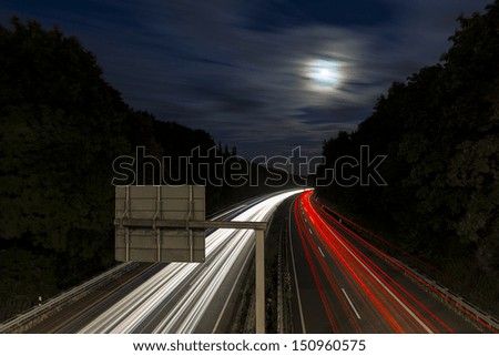 long time exposure on a highway with car light trails and moon in the sky