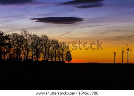 Age tree silhouette with wind farm in the sunset and energy pinwheel in the winter