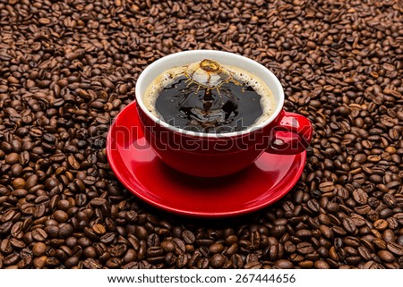 red cup of hot coffee with drop collision Liquid Art on brown beans