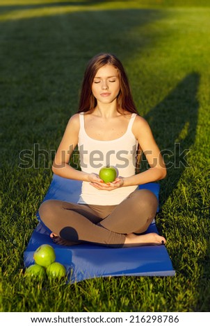 Young girl sitting on yoga mat and holding an apple while outdoors in a park