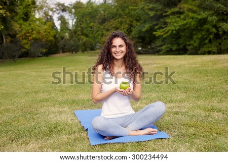 woman holding apple and sitting on the yoga-mat. Outdoor