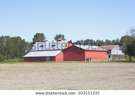 A big red barn stands before an unseeded field/Unseeded Field and Red Barn/An unseeded field ready for plowing