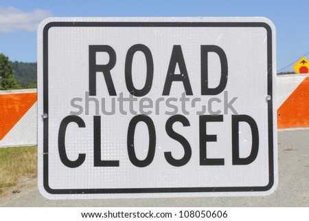 A sign warns that the road up ahead is closed/Road Closed Sign/A metal sign in bold capitol letters warns that the road is closed up ahead.