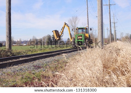 A machine is used to cut and trim vegetation growing beside railway tracks/Railway Track Maintenance/A machine is used to cut and trim vegetation growing beside railway tracks