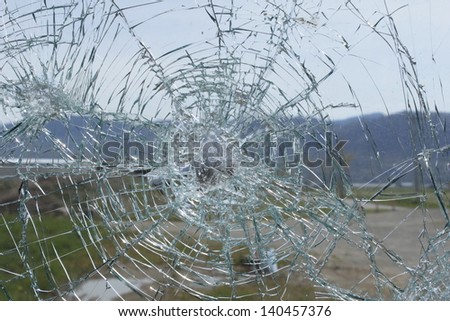 An errant rock has shattered glass/Shattered Glass/A vandalized window after someone has tossed a rock.