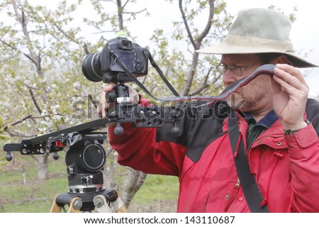 A videographer uses a portable dolly to record a scene in an orchard/Videographer Shooting Nature/A videographer uses a portable dolly to record a scene in an orchard