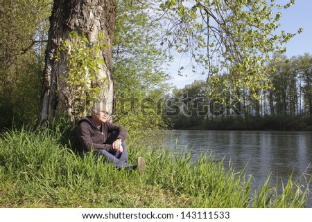 An older man rests beside a river/Retired Man by River/An older man rests beside a river.