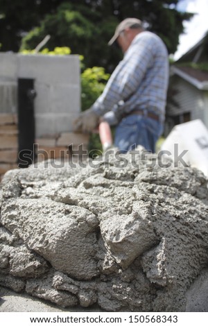 A mason applies cement to a brick wall/Mason at Work/A mason applies cement to the exterior brick wall bordering a private residence.