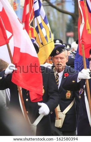 ABBOTSFORD, BRITISH COLUMBIA/CANADA -Â?Â? NOVEMBER 11: A war veteran carries the Canadian flag during Remembrance Day ceremonies in Abbotsford, British Columbia on November 11, 2013.