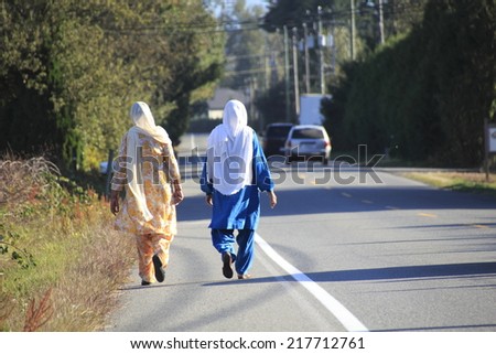 Two Sikh women walk together on a rural road/Two Sikh Friends Walk on Rural Road/Two Sikh women walk together on a rural road