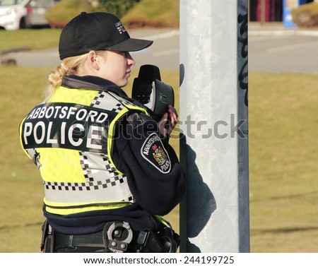 ABBOTSFORD, BC/CANADA - JANUARY 10, 2015:A female police officer holds a radar gun checking for speeding vehicles in Abbotsford, BC, Canada on January 10, 2015. .