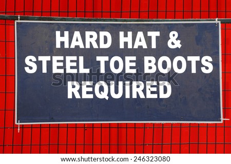 A sign on a construction site requires a hard hat and steel toe boots/Hard Hat and Boots Required Sign/A sign on a construction site requires a hard hat and steel toe boots.