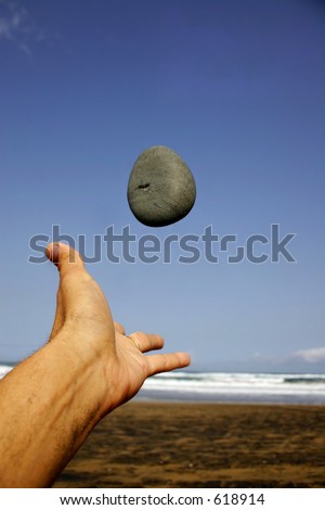 Hand throwing pebble into the air on the beach