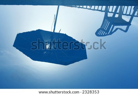 Reflection of parasol and chair in still blue water