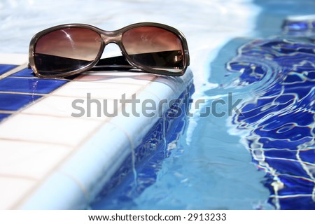 Sunglasses by bright swimming pool with mosaic pattern