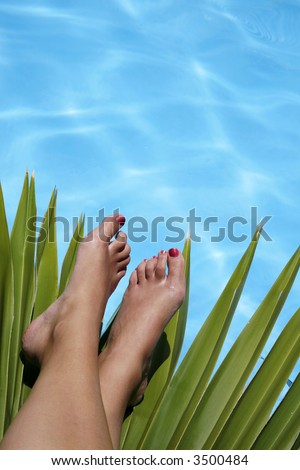 Feet resting on tropical foliage by blue pool