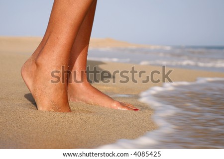 Woman standing  on a golden beach with waves at her feet