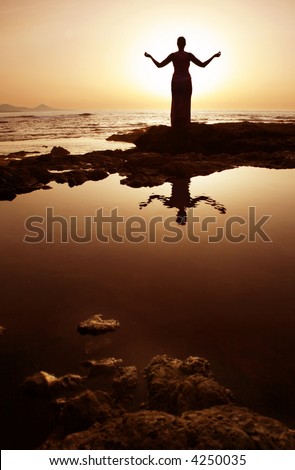 Woman in meditation pose at sunset with reflection in water