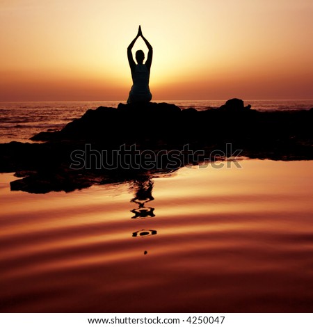Woman doing yoga at sunset on the seashore