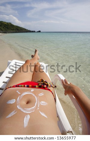 Pretty woman lying on the beach with sun drawn in suntan cream on her stomach