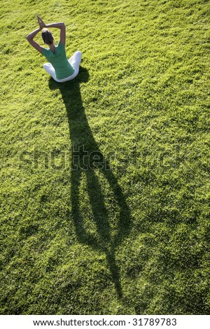 Woman meditating on green grass with a long afternoon shadow