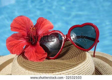 Fuky sunglasses on a summer hat with a red tropical hibiscus flower and nice blue pool water
