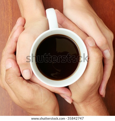 Four hands wrapped around a cup of coffee