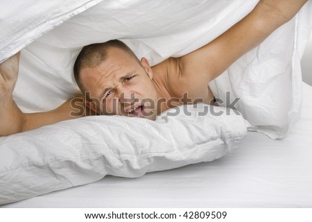 Confused man waking up in bed with a sheet over his head