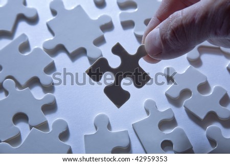 Hand holding a piece of a jigsaw puzzle, silhouetted against a background of more puzzle pieces