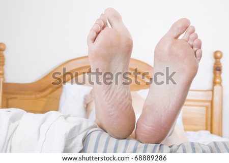 A woman\'s feet at the end of a bed with a striped duvet