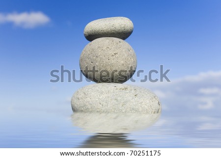 Stack of zen pebbles reflected in still water with a blue sky behind.