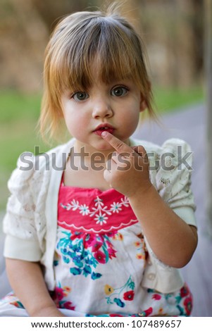 Cute toddler portrait in outdoor park saying be quiet looking into the camera. Shallow depth of field focusing on eyes and face.