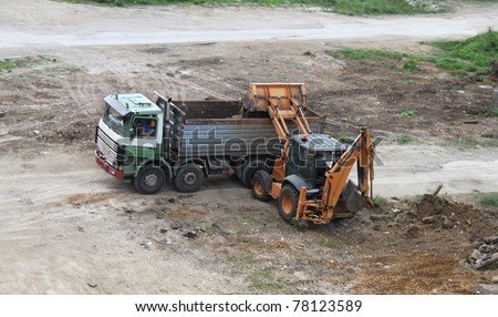 Excavator loading dirt on truck. Earth moving equipment at construction work