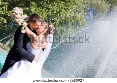 a bride bouquet of flowers and a groom kissing near the fountain