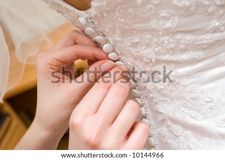 hands of a person help to a bride to clasp buttons of the dress