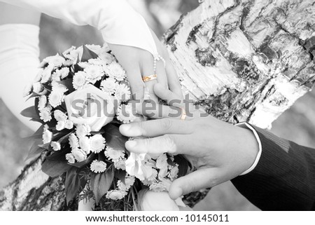 hands of the bride and groom over the flower bouquet in black and white