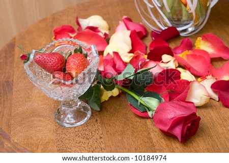 strawberry in a vase, red rose on the table and petals of red roses