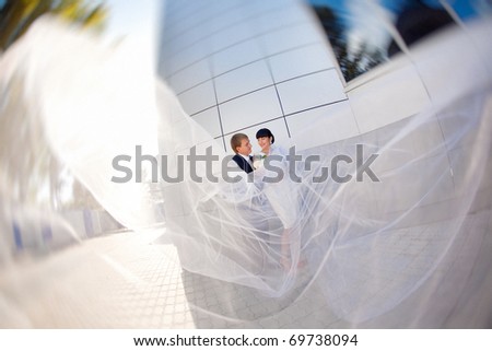 bride and groom by the wall with long flying veil