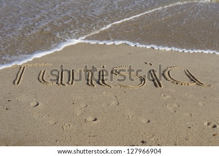 The word Tunisia written in sand with waves lapping at the beach