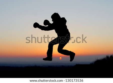 Boy in boxing gloves in silhouette with orange and red sunset sky