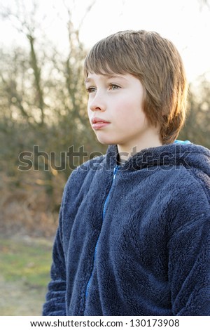 Young male boy looking ahead in serious pose, wearing outdoor clothes and sunset background