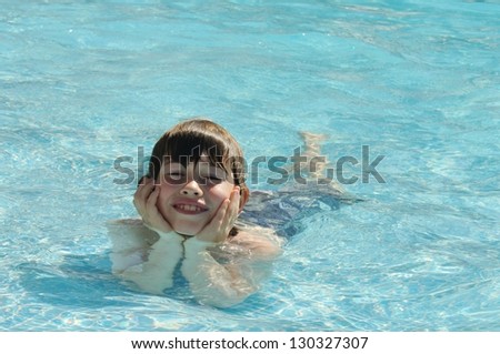 Boy laying in swimming pool with chin resting on hands in relaxed and happy pose