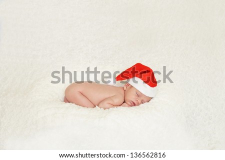 Festive image of newborn baby in natural foetal sleeping position on white blanket with red Santa hat on.