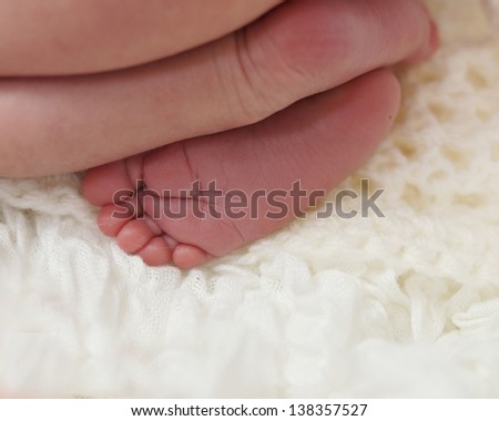 Tiny newborn baby feet crossed over, on soft background
