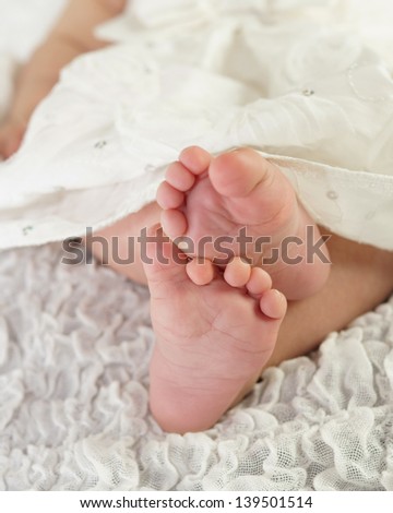 Close up of baby\'s feet crossed over, with pretty white dress showing.