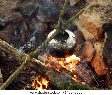 Metal kettle boiling over open fire pit in outback setting