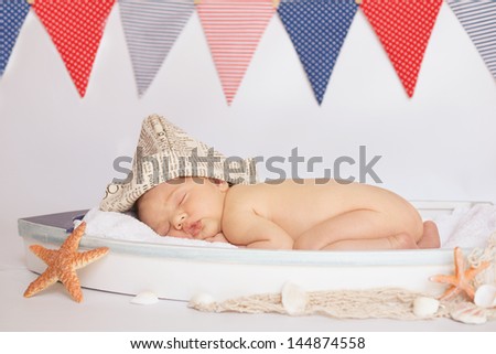 Newborn baby in sailing hat asleep in tiny boat. Nautical theme