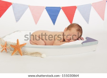Sleeping newborn baby  in tiny wooden boat with nautical theme