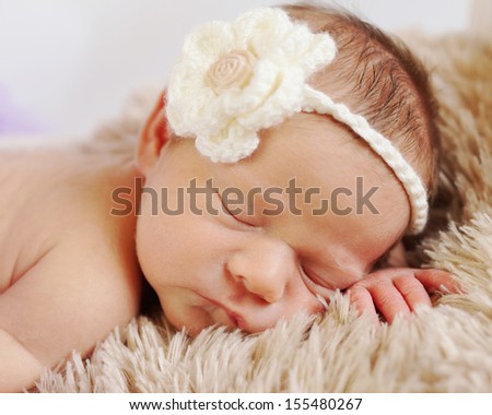 Sleeping newborn baby on fluffy beige blanket with cream flower headband on
